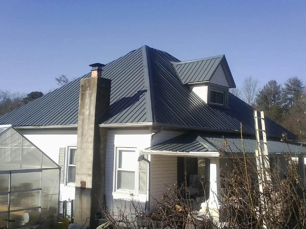 Dark blue standing seam metal roof on a white farmhouse with dormer — Slate & Tile Roof Repair by Roofing Brothers in Long Pond