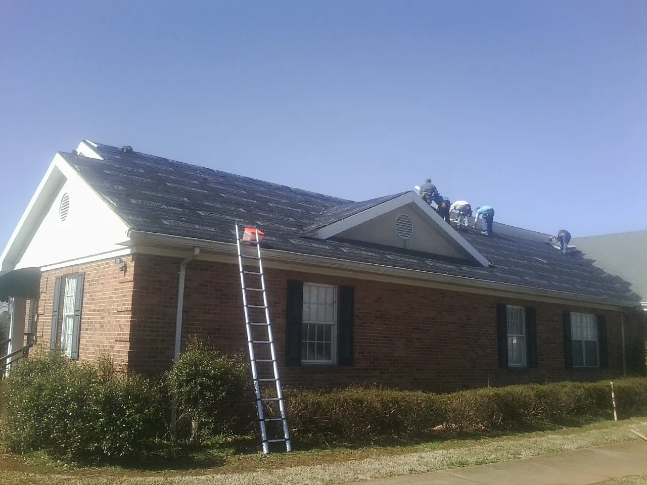 Crew tearing shingles off a brick ranch roof with a ladder set — Emergency Roof Repair work by our crew in Long Pond