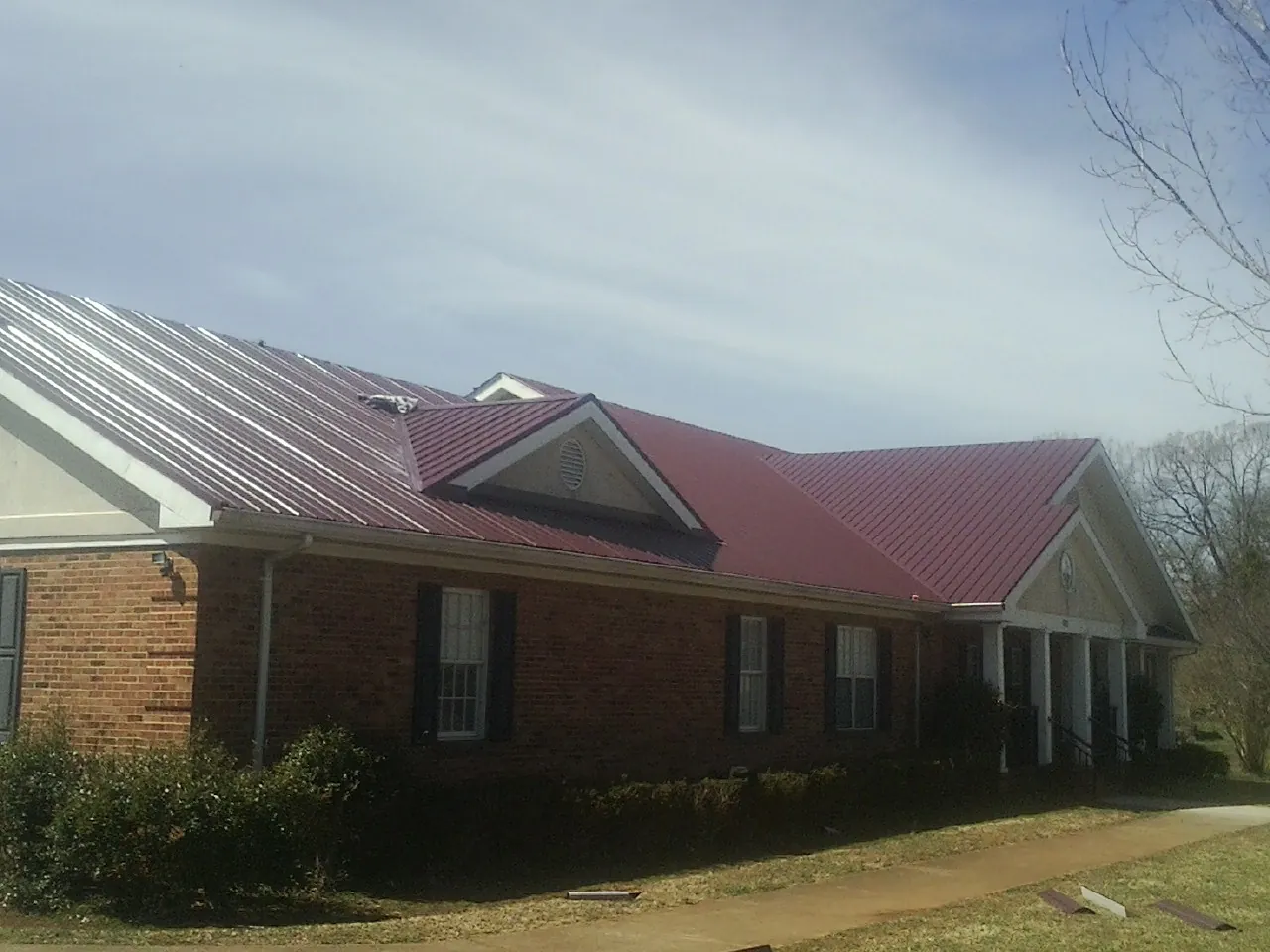 Red metal roof with gabled entries on a long brick building, from a Hail Damage Roof Repair job in Long Pond