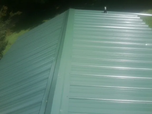 New green metal panels meeting at the ridge of a roof — Flat Roof Repair work by our crew in Long Pond