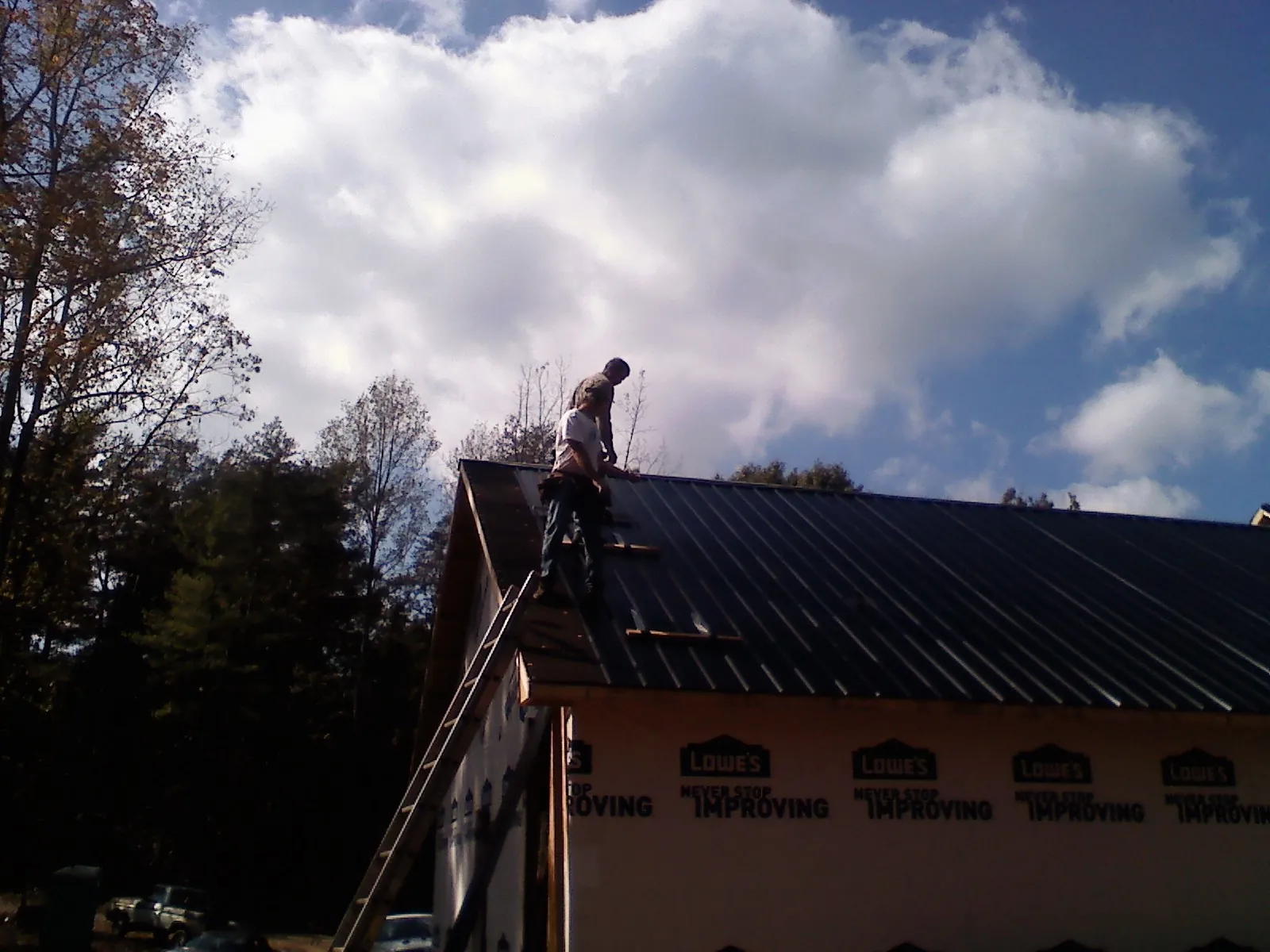 Roofer fastening dark metal panels high against a cloudy sky, from a Roof Inspection job in Long Pond
