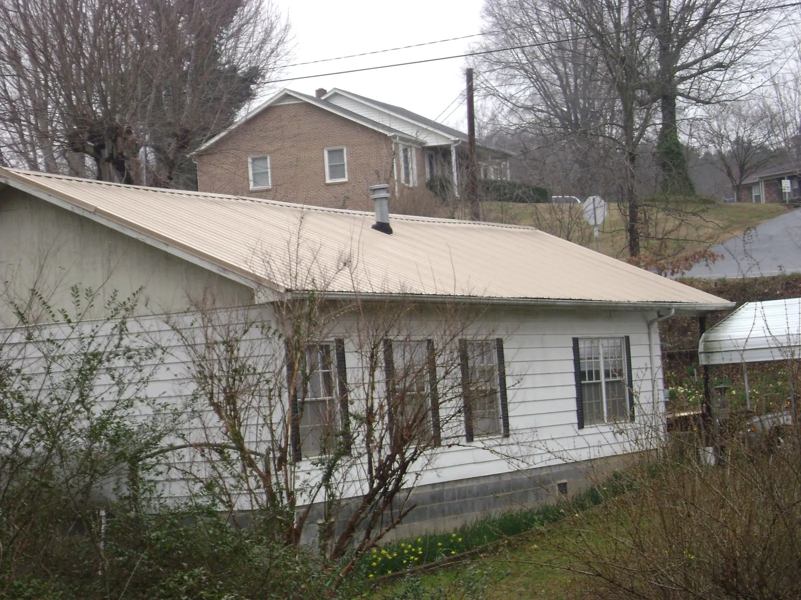 Tan metal roof on a white sided house set into a hillside — Commercial Roofing by Roofing Brothers in Long Pond