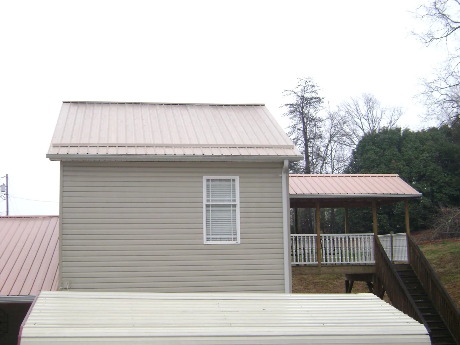 Tan metal roofs on a two story addition and attached porch, from a Roof Replacement job in Long Pond